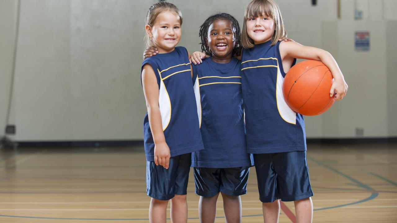 Three young girl basketball players smile while hugging