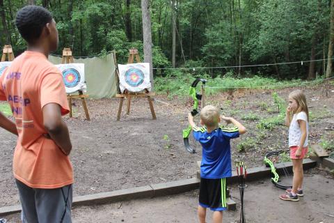 two children archery target practice with staff supervision at summer camp